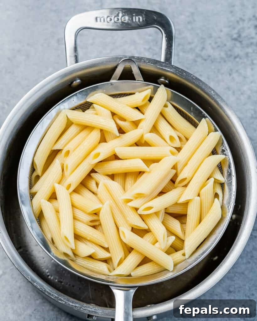 Cooked penne pasta draining in a colander, cooling off before being added to the sauce.