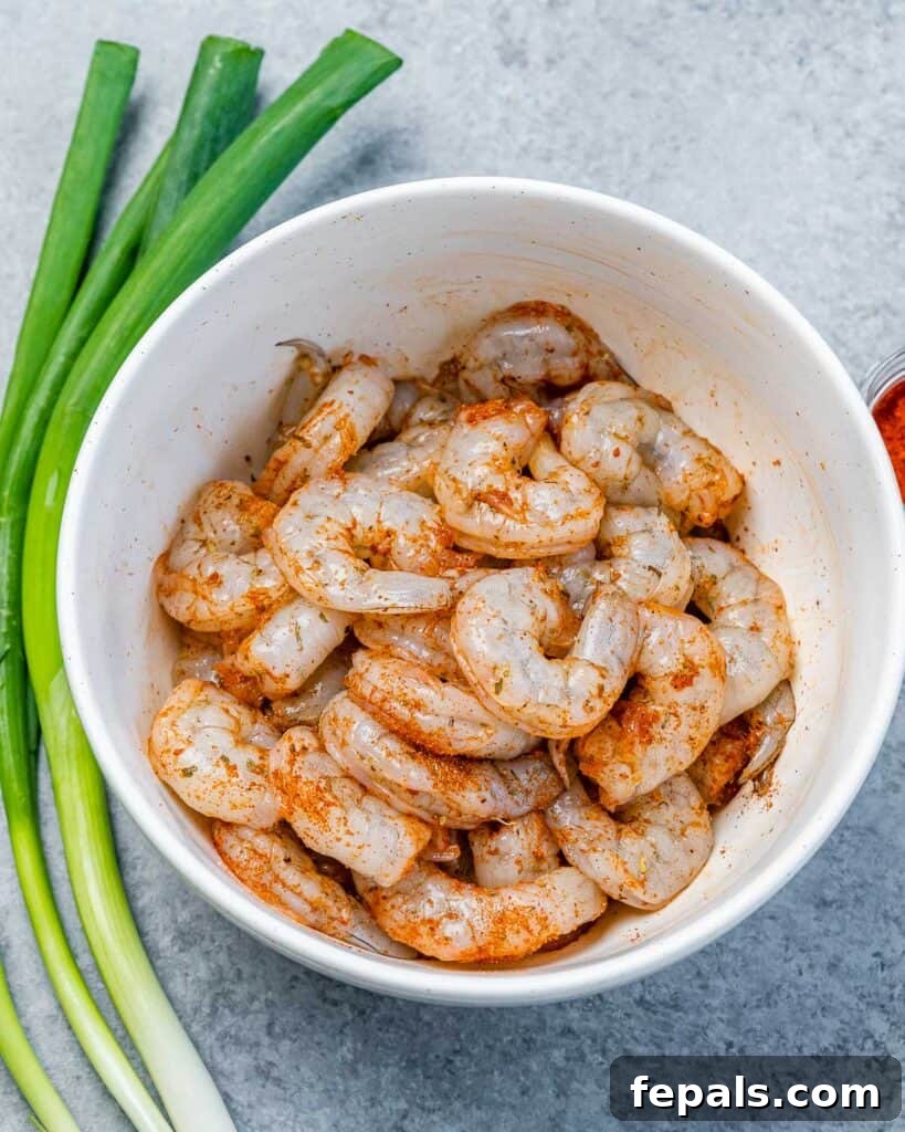 Raw jumbo shrimp seasoned with jerk seasoning in a round white bowl, ready for cooking.