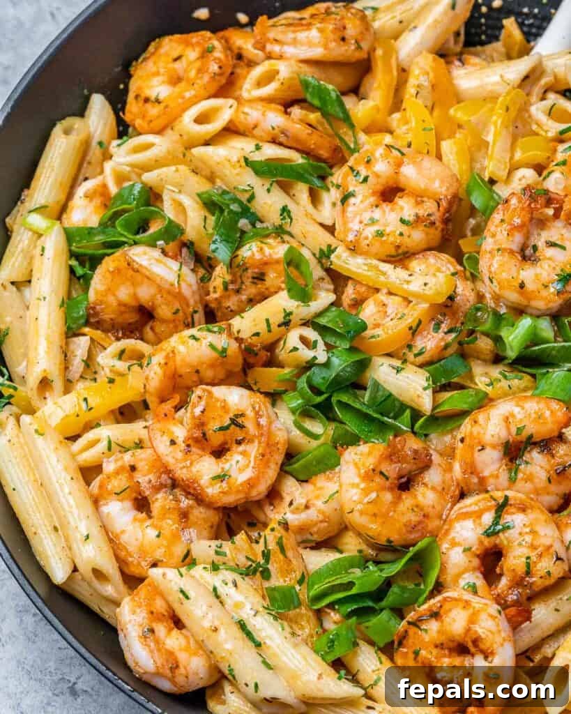 Top close-up view of creamy, orange-colored Rasta Pasta with shrimp, garnished with sliced green onions, highlighting the texture and richness.