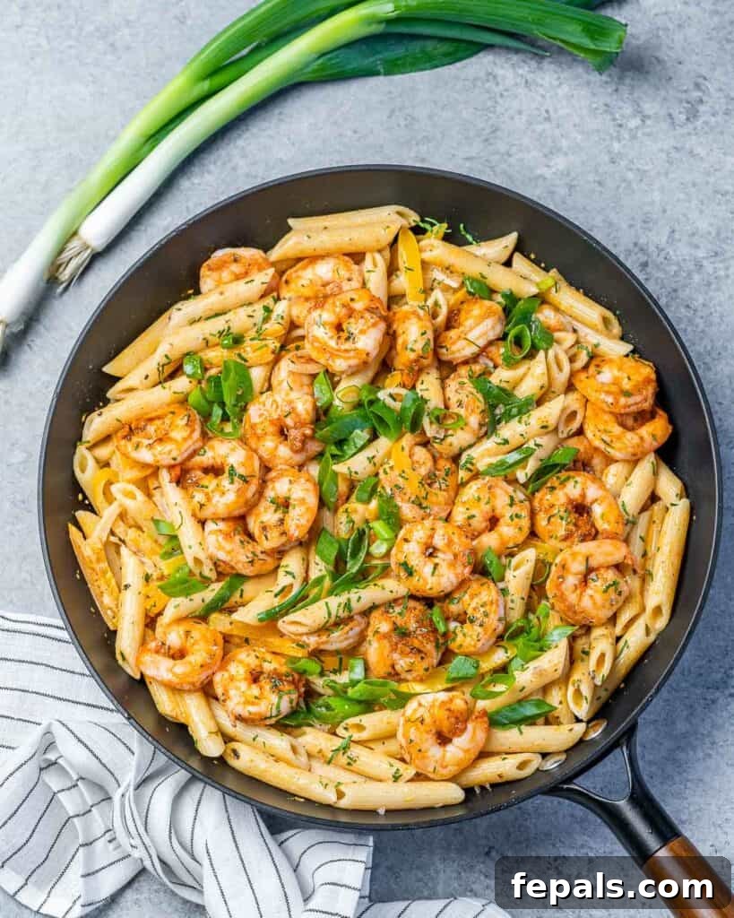 Top view of a black skillet featuring creamy, orange-hued Shrimp Rasta Pasta with green onions, ready to be served.