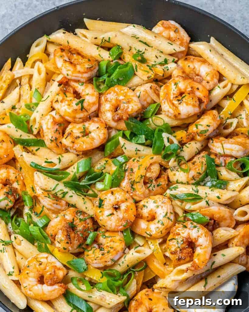 Top close-up view of a black skillet showcasing creamy Shrimp Rasta Pasta garnished with sliced green onions, ready for serving.