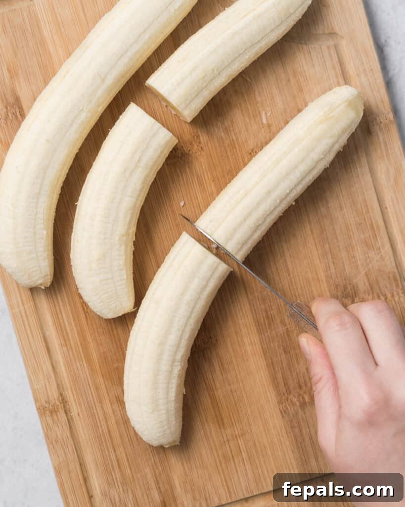 Frozen Chocolate Banana Bites 5 hand cutting peeled banana in half on a cutting board