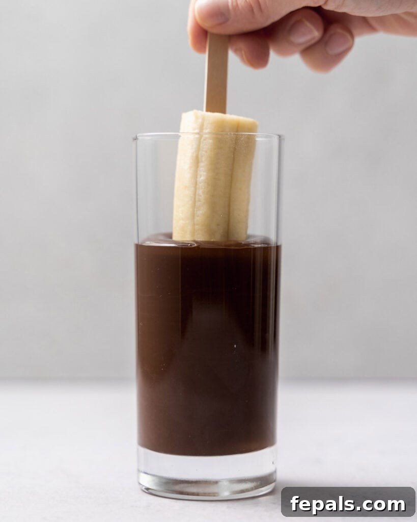 Frozen Chocolate Banana Bites 9 banana pop being dipped into a cup of melted chocolate