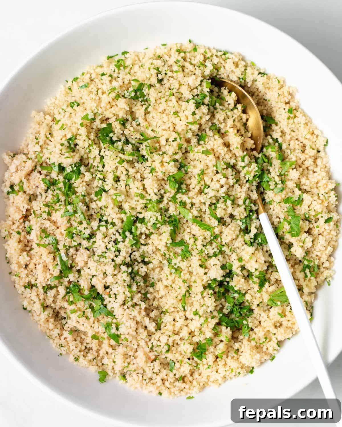 Top view of a round plate of cooked couscous with chopped parsley and spoon on plate over couscous.