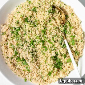 top view of a round plate of cooked couscous with chopped parsley and spoon on plate over couscous