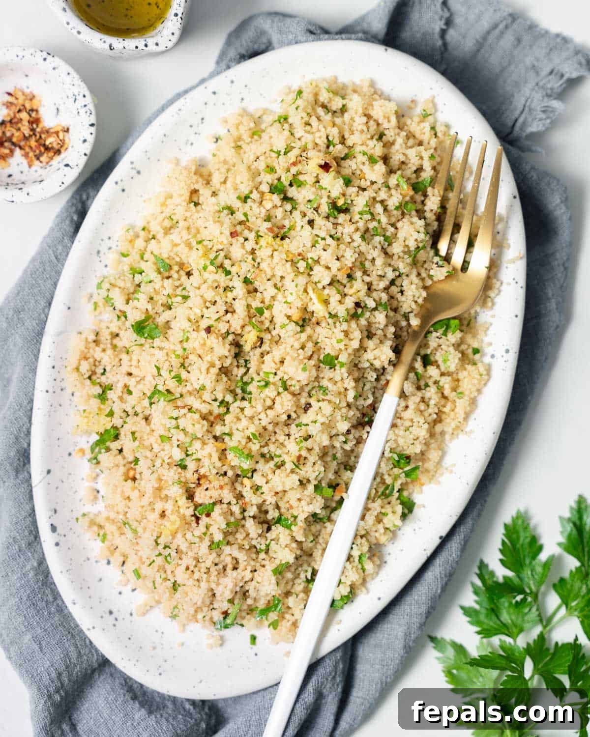Couscous with fresh parsley on a white serving platter with a fork.