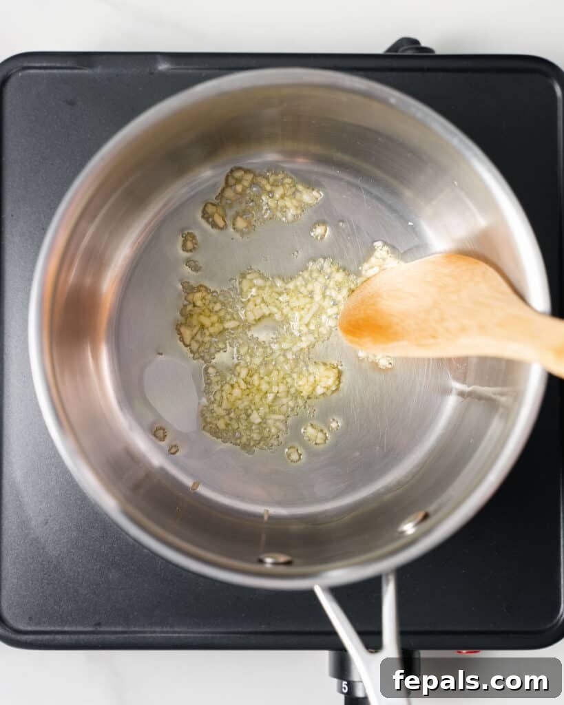 Using a wooden spoon to stir garlic in a pot with oil.