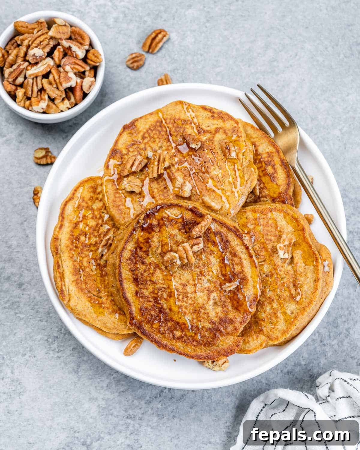 Top view of fluffy sweet potato pancakes on a plate topped with pecans and maple syrup, with a fork resting beside them.