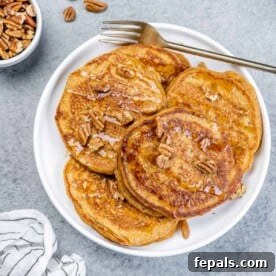 top view of pancakes on a plate topped with pecans with fork by pancakes