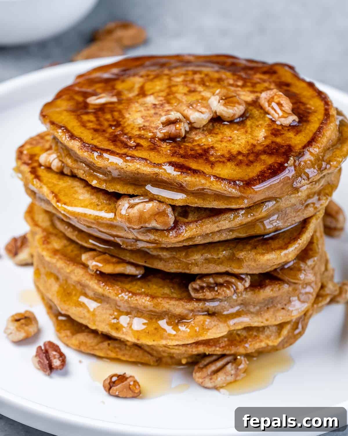 Closeup view of a tall stack of sweet potato pancakes generously topped with golden maple syrup and crunchy pecans.
