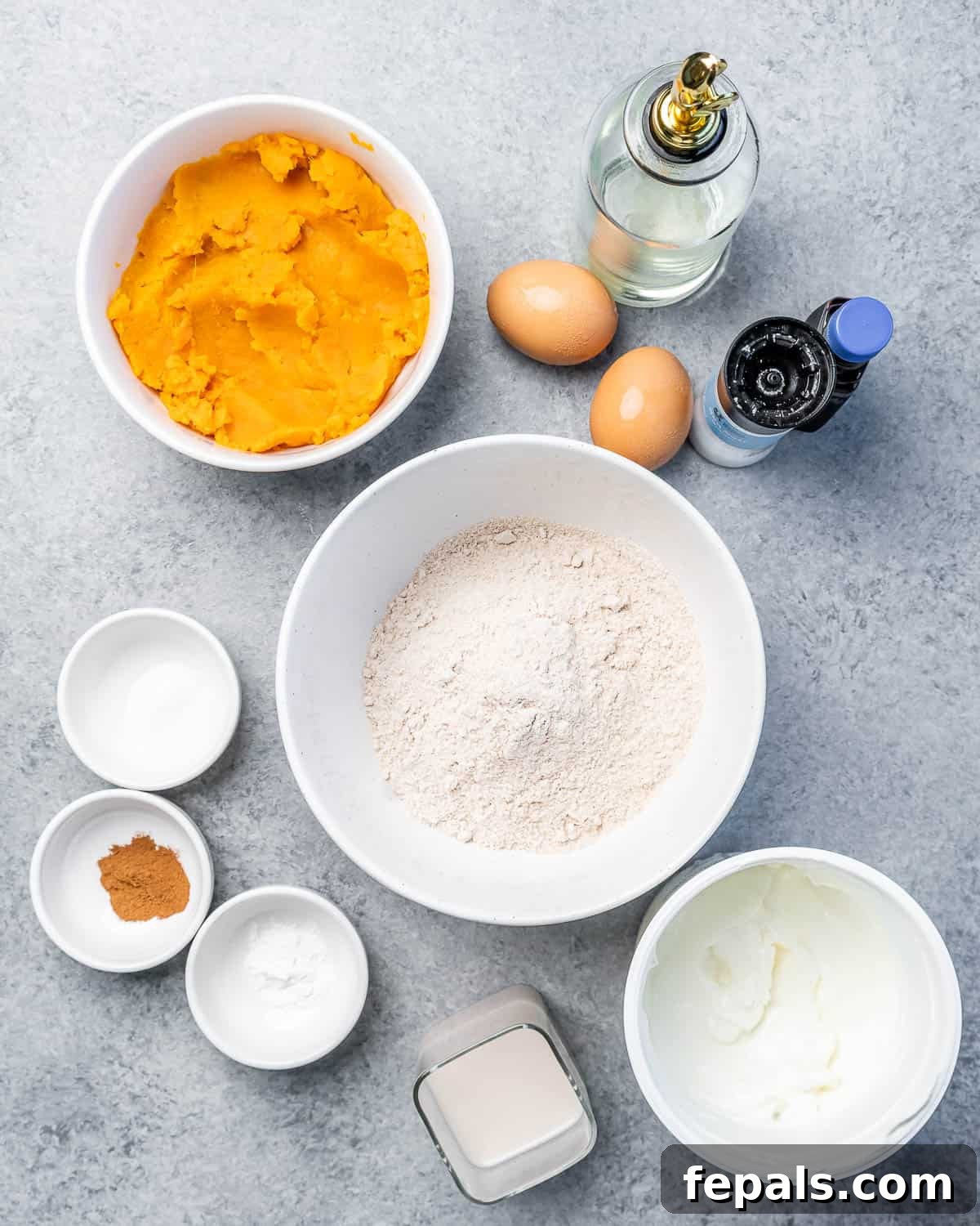 Close-up of the key ingredients laid out: whole wheat flour, mashed sweet potato, eggs, vanilla extract, and vegetable oil, ready for mixing.
