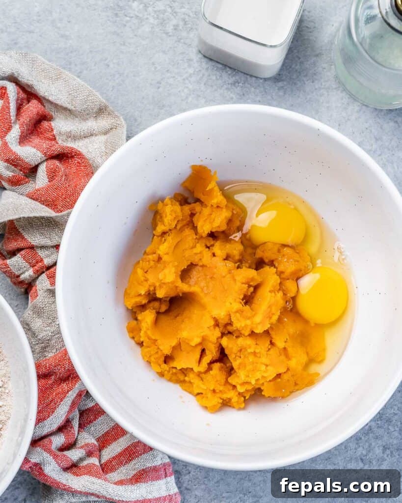 A large white bowl filled with creamy mashed sweet potatoes and cracked eggs, illustrating the start of combining wet ingredients.