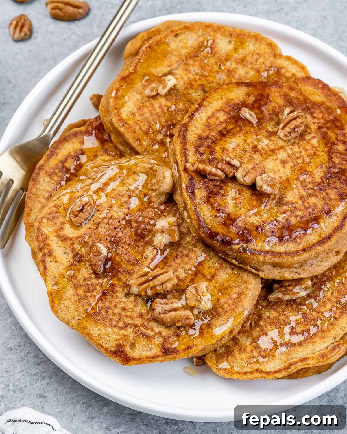 A perfectly cooked sweet potato pancake on a white plate, garnished with chopped pecans and resting next to a fork, ready to be enjoyed.