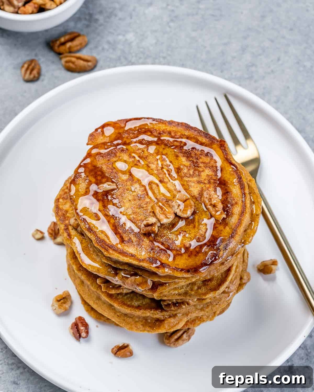 Top view of a beautifully arranged stack of sweet potato pancakes, generously drizzled with maple syrup and adorned with scattered chopped pecans.