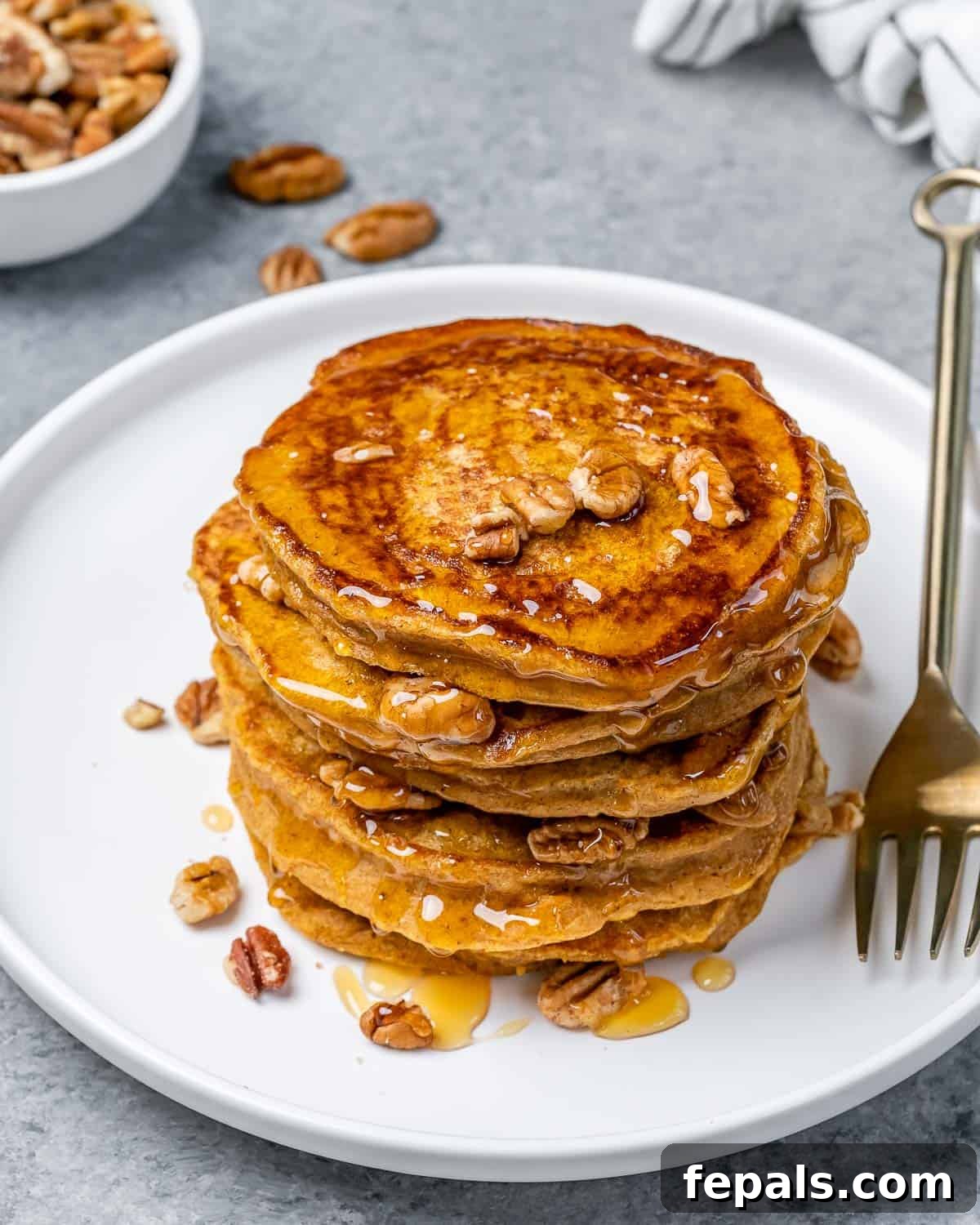 A stack of perfectly cooked sweet potato pancakes presented on a white plate, accompanied by a fork, ready to be enjoyed.