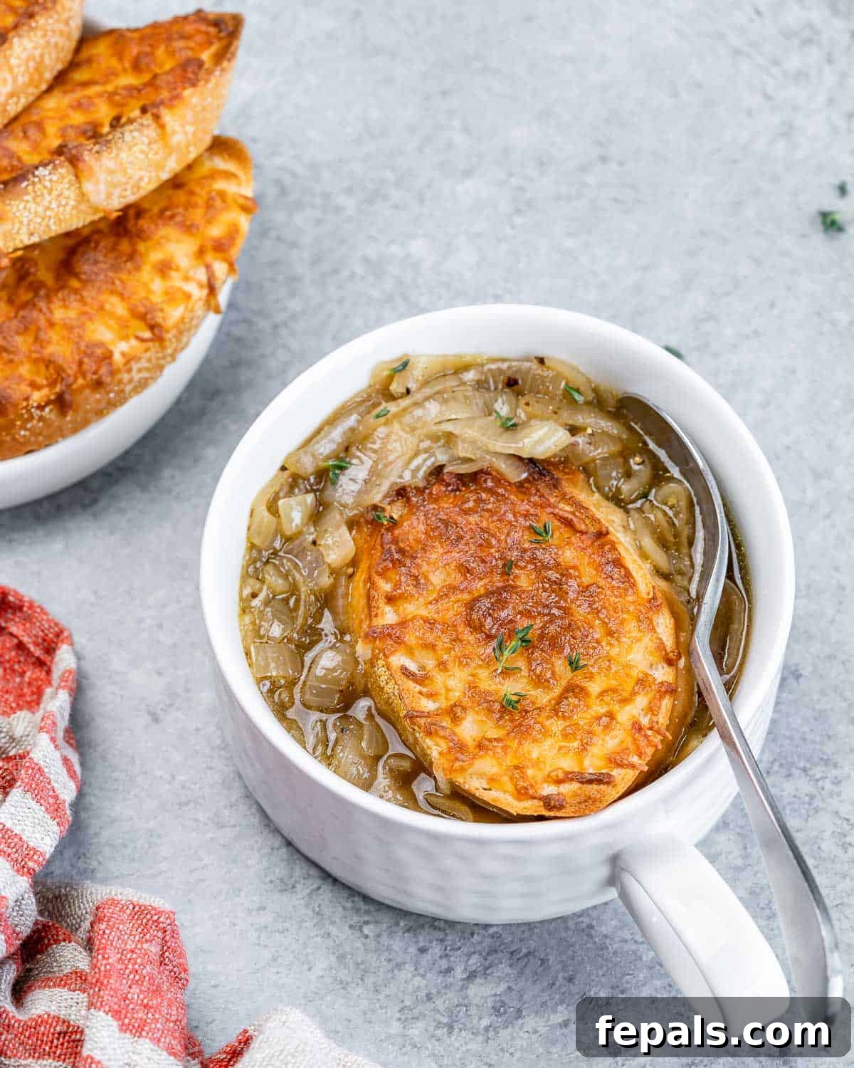 Effortless French Onion Elegance 3 Spoon in a bowl of soup with onions and a toasted baguette.