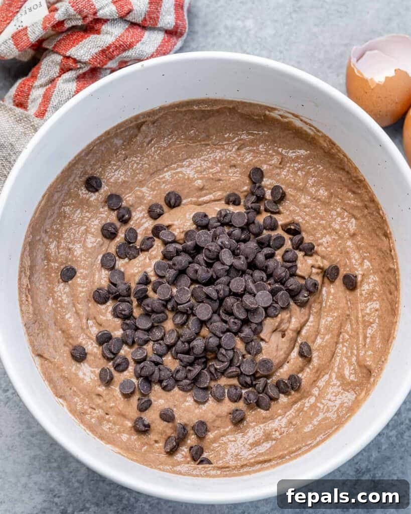 Mini chocolate chips added over chocolate waffle batter in a round bowl, waiting to be folded in.