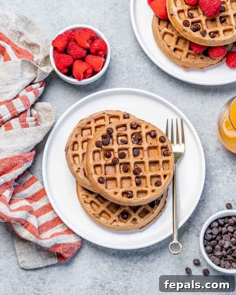 Chocolate waffles on a plate with a fork on the right side, topped with mini chocolate chips and ready to be eaten.