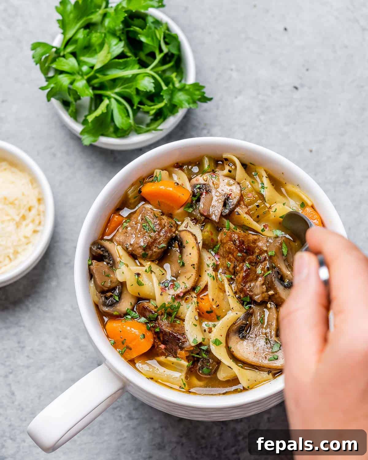 Hearty Beef Noodle Comfort 9 Woman's hand stirring soup in a bowl.