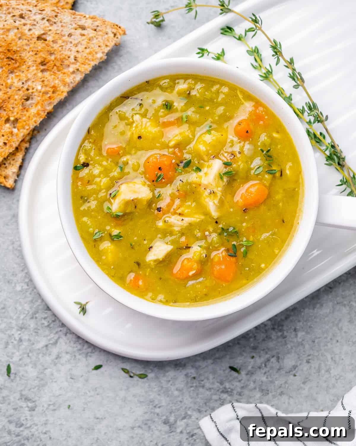 Top view of a white round bowl of slow cooker split pea soup with chicken, garnished with fresh parsley.