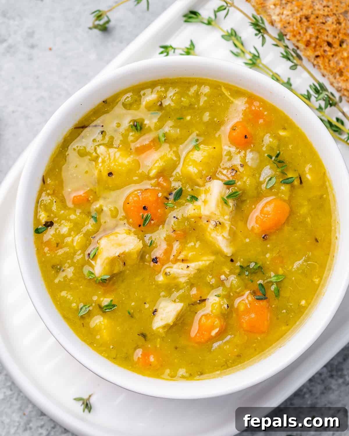 A closeup view of a white bowl filled with creamy split pea soup, garnished with parsley.