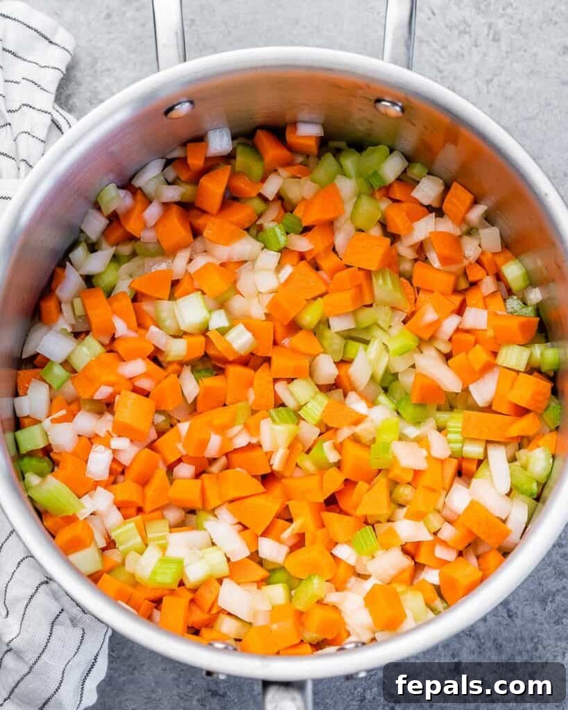 Diced carrots, onion, and celery sautéing in a large pot with olive oil.