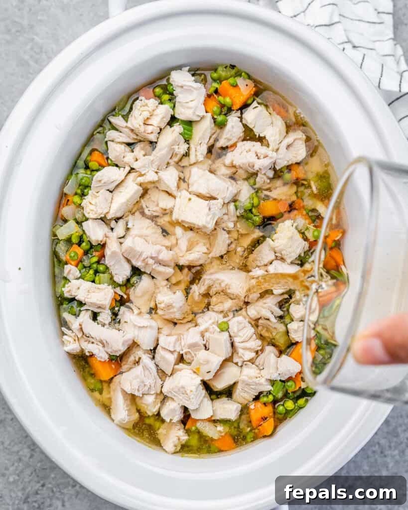 Pouring chicken broth into the slow cooker over vegetables and chicken.