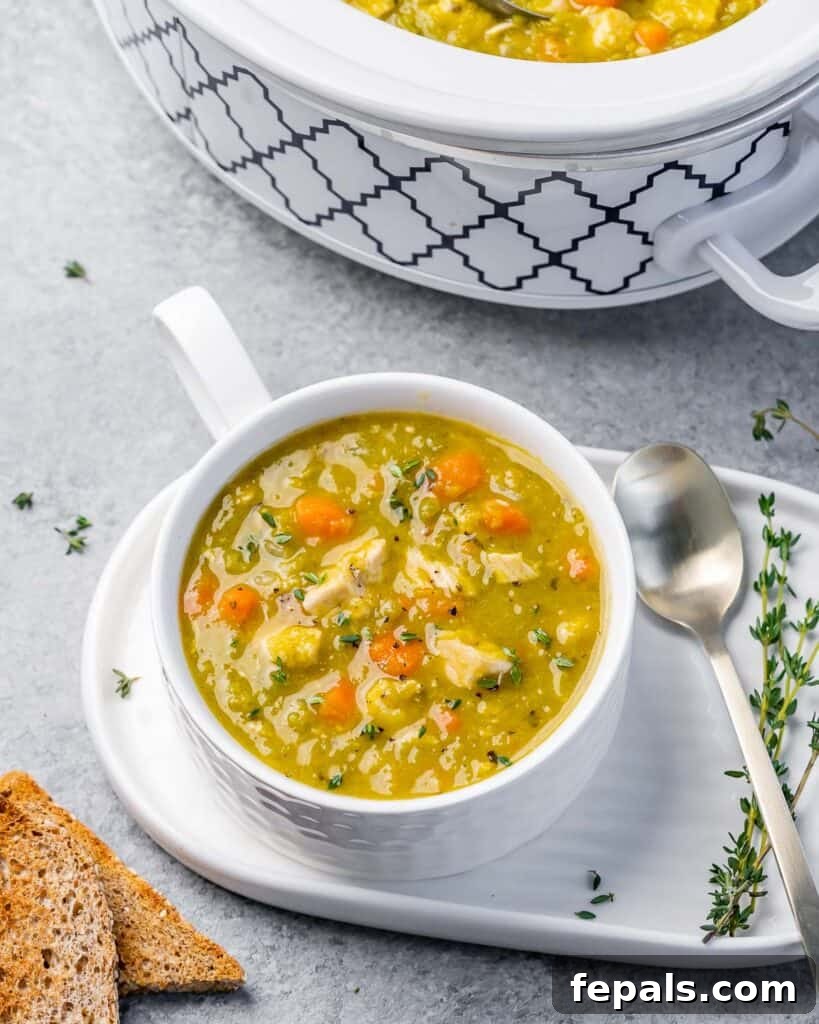 A close-up side view of a white bowl filled with split pea soup, showcasing the chicken and carrots, on a rustic wooden surface.