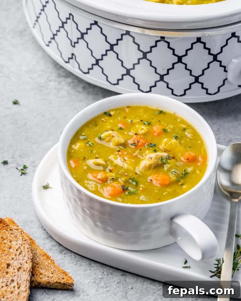A side shot of a white mug filled with slow cooker split pea soup next to a slow cooker.
