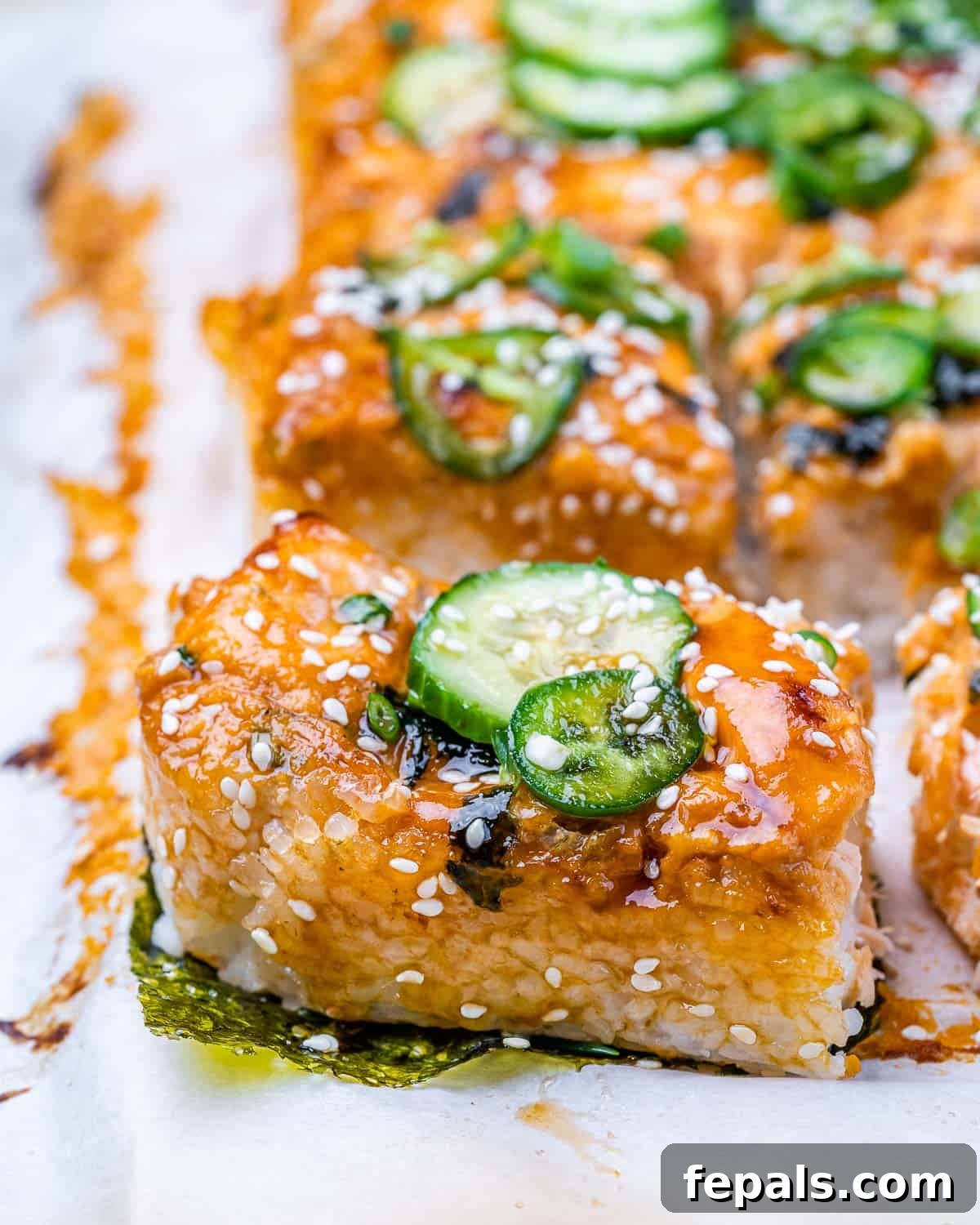 Ultimate Salmon Sushi Bake 3 Side shot of a sushi bake cut into servings and topped with sliced cucumber and jalapeños.
