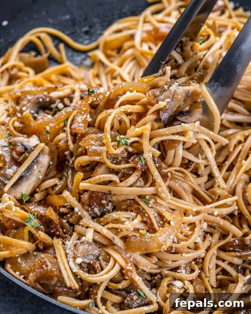 Golden Caramelized Onion Pasta 8 A pair of tongs expertly tossing French onion pasta in a large pan, mixing the noodles with the rich, savory sauce.