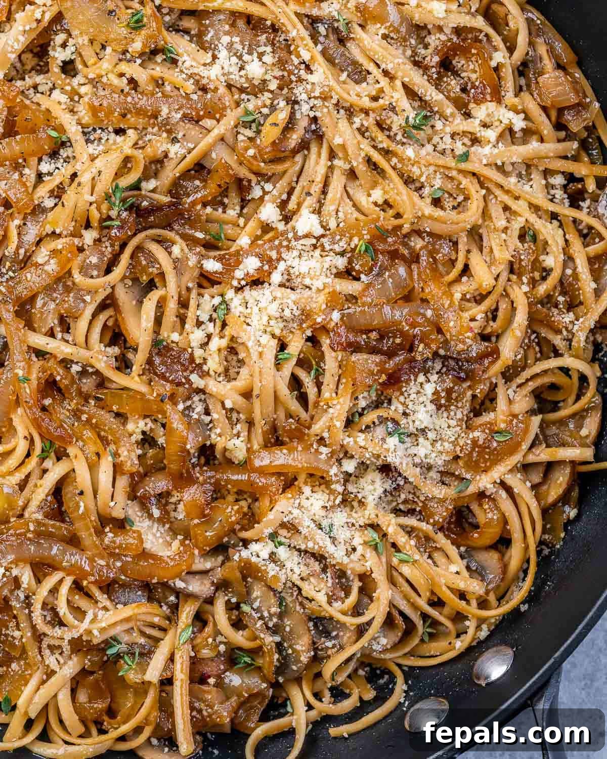 Caramelized Onion and Gruyere Pasta 10 Closeup view of pasta made with onions and mushrooms, topped with Parmesan cheese and fresh herbs.