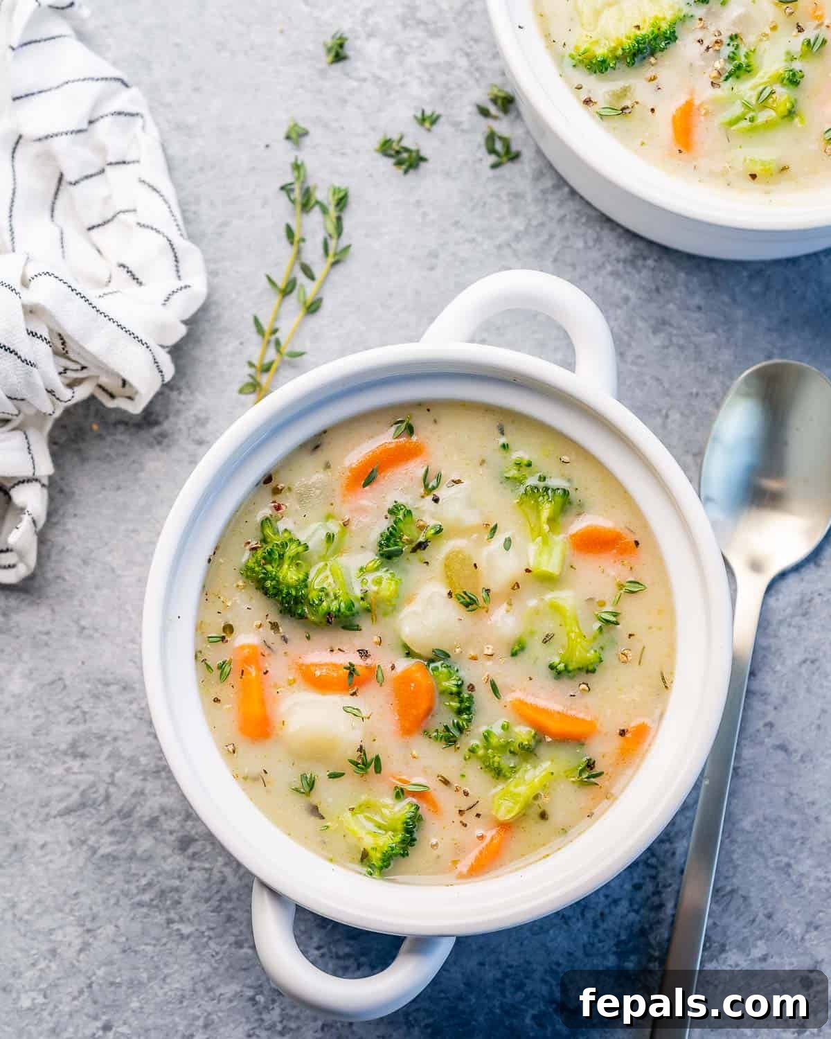 Top view of a white round bowl of creamy vegetable soup, garnished with fresh herbs.