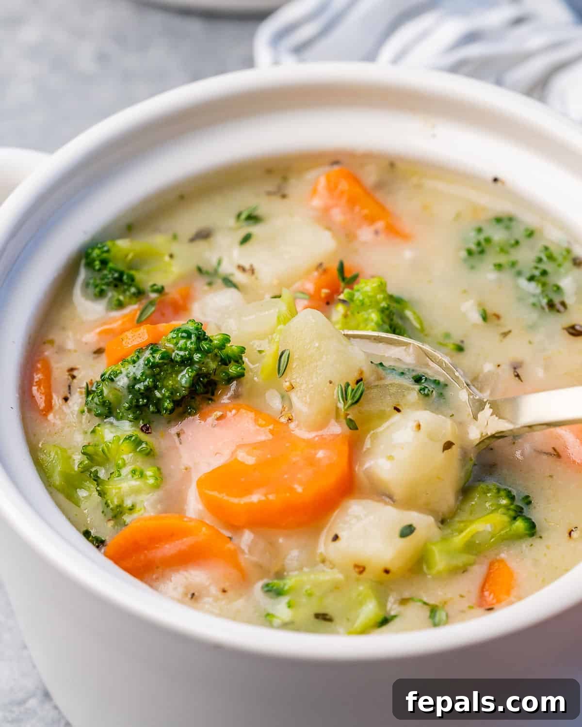 Close side view of a spoon stirring creamy vegetable soup in a white bowl, showing its rich texture.