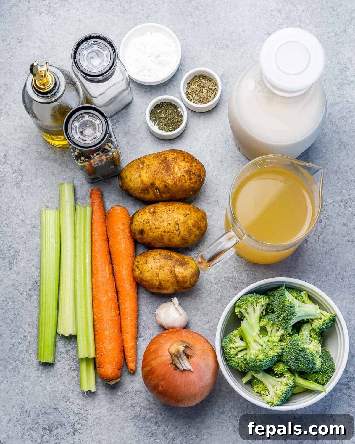 A vibrant flat lay of all raw ingredients: potatoes, carrots, celery, broccoli, onion, garlic, vegetable stock, and seasonings arranged on a wooden board.