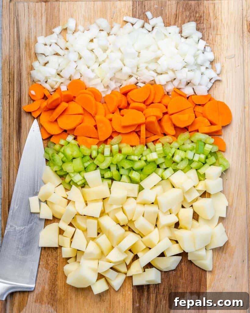 Chopped carrots, celery, onion and potatoes on a cutting board, ready for cooking.