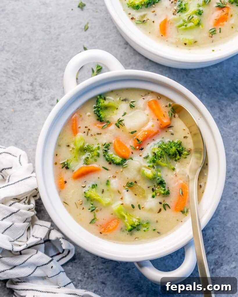 Top view of a round white bowl of creamy vegetable soup with a spoon resting inside.