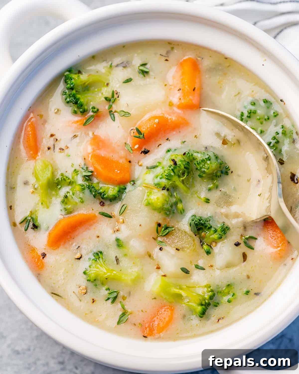 Close-up of creamy vegetable soup in a white bowl, showing broccoli, carrots, and potatoes in the rich broth.