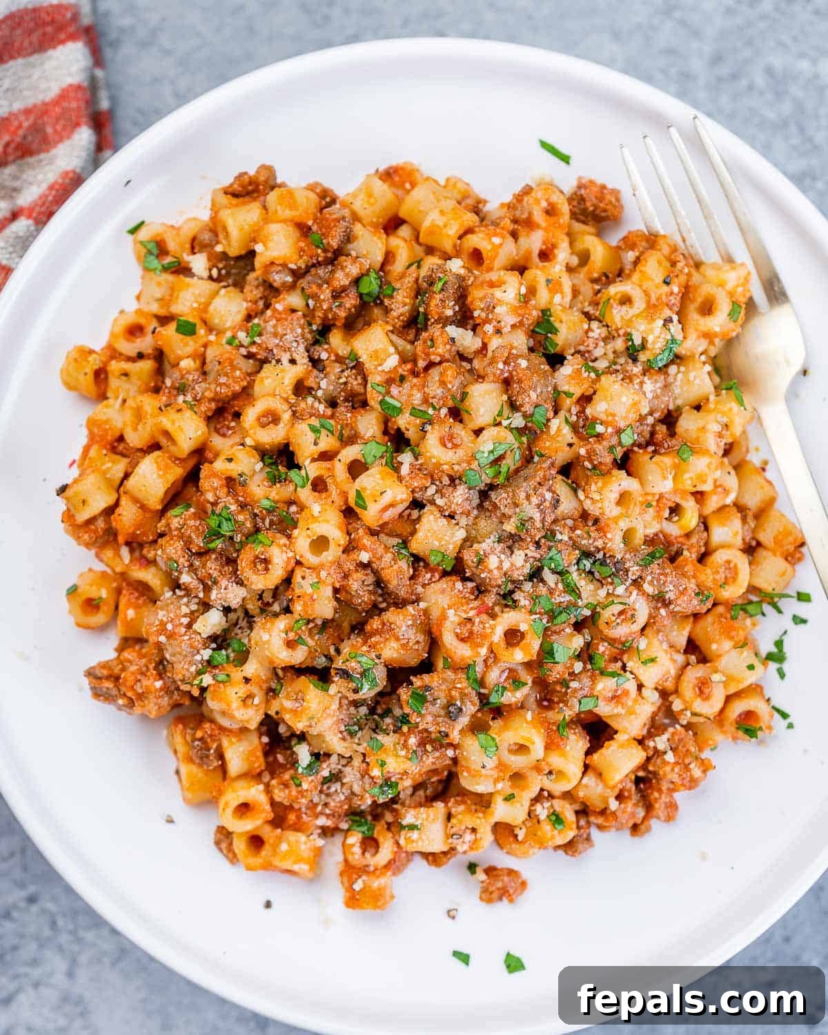 Creamy Cottage Cheese Pasta 2 Top view of a round white plate with short pasta with red sauce, garnished with fresh herbs.