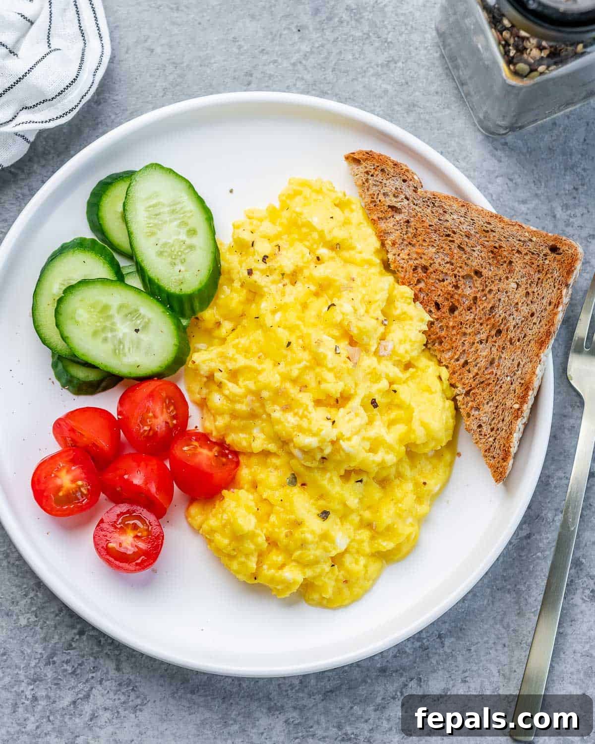 Creamy Protein Scramble 2 Top view of scrambled cottage cheese eggs with toast, chopped cherry tomatoes and sliced cucumber.