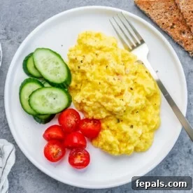 Creamy Protein Scramble 11 scrambled cottage cheese eggs with chopped cherry tomatoes and sliced cucumber on the left of the scrambled eggs.
