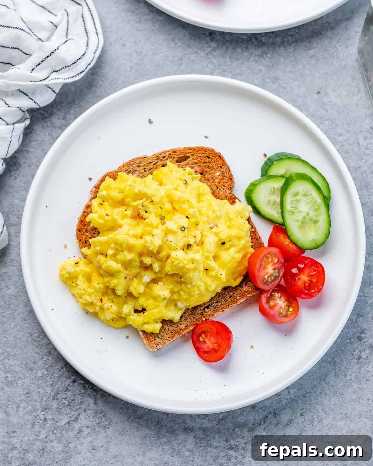 Creamy Protein Scramble 8 Scrambled eggs served on toast with a side of sliced cucumbers and grape tomatoes.