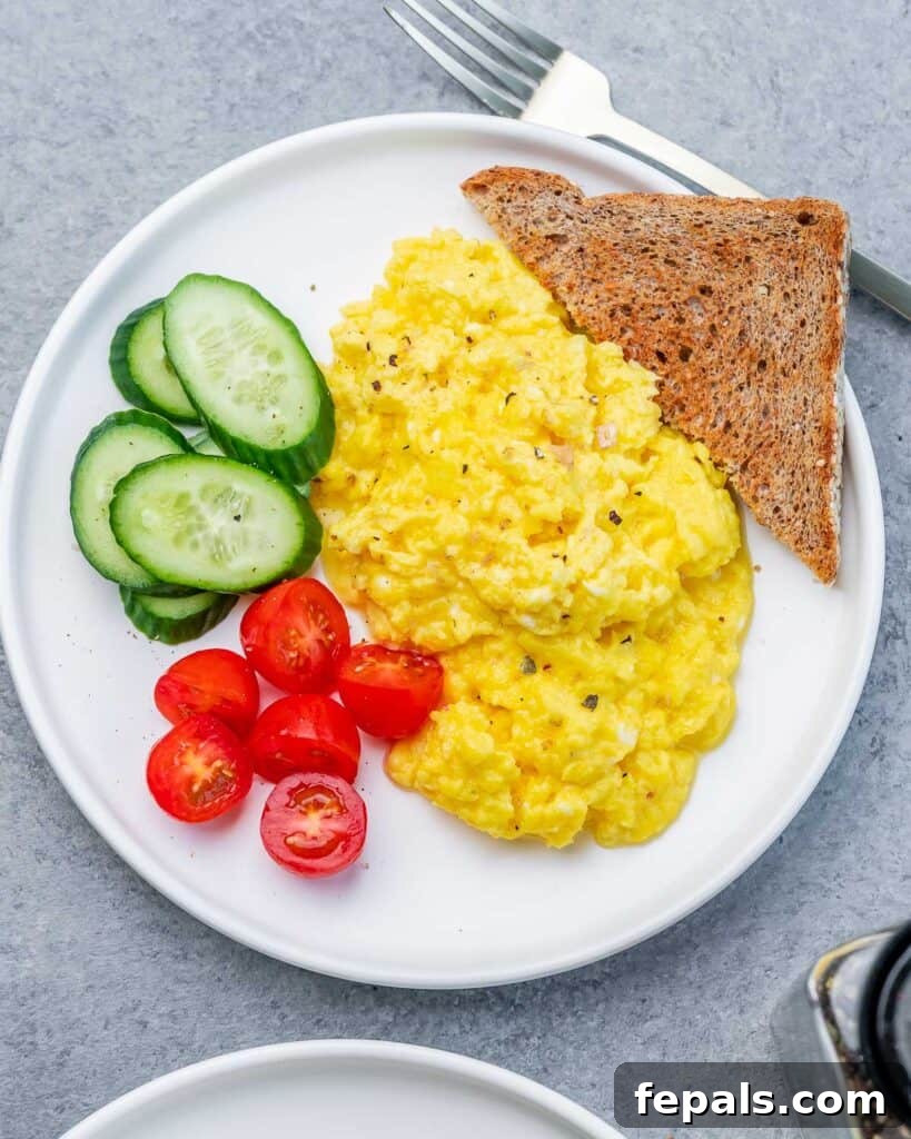 Creamy Protein Scramble 9 top view of a plate with scrambled eggs, sliced tomatoes, sliced cucumbers with a while grain toast bread by the eggs