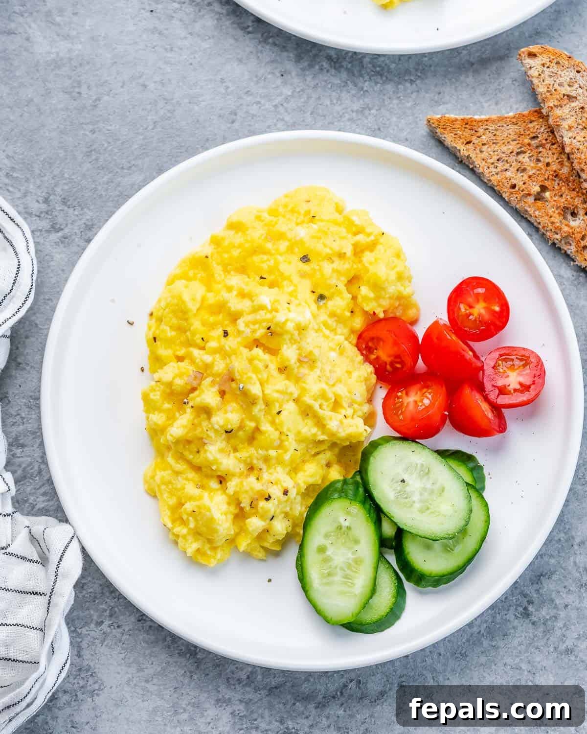 Creamy Protein Scramble 10 Cottage cheese eggs on a white plate with cucumbers and tomatoes.