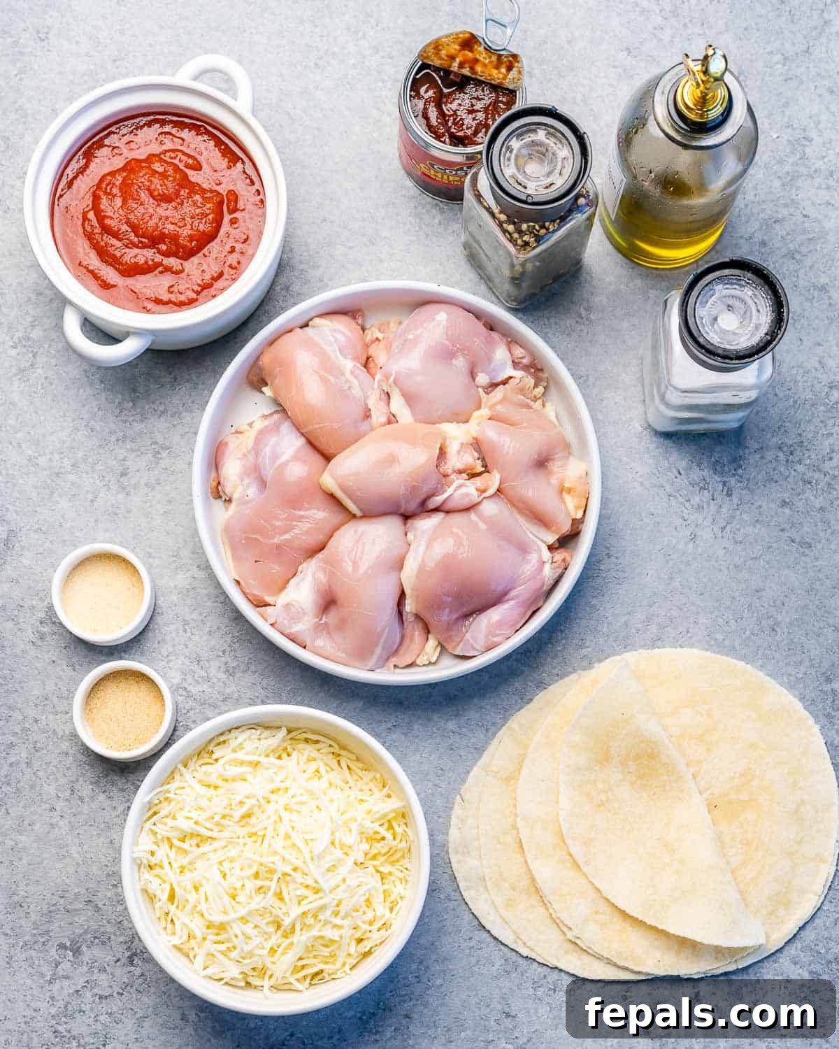 Crispy Birria Chicken Dipping Tacos 4 Çiğ tavuk, tortillalar, rendelenmiş peynir, domates sosu ve çeşitli baharatlar mutfak tezgahına serilmiş.