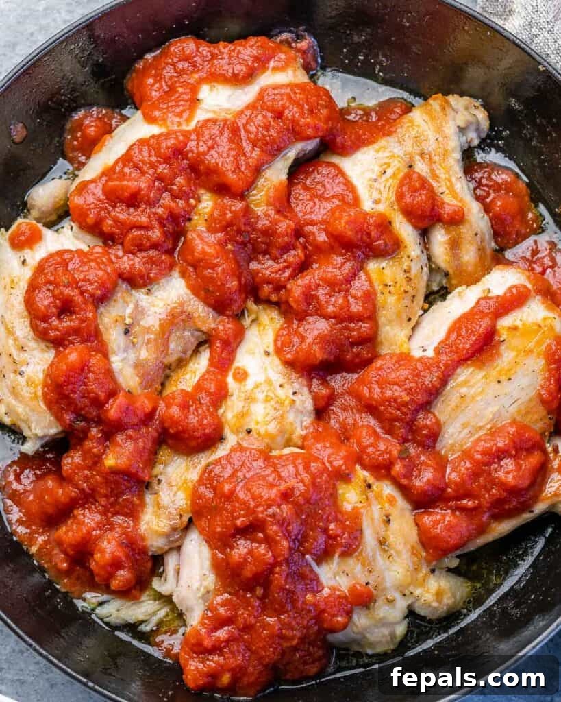 Crispy Birria Chicken Dipping Tacos 6 Kırmızı adobo soslu tavuk butları bir tavada pişiyor, fırına hazır.