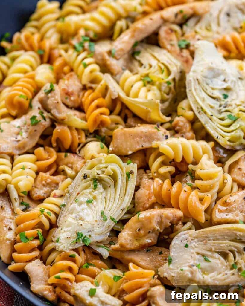 Creamy Chicken Artichoke Delight 9 close up image of multi-colored pasta in a pan with artichoke and chicken