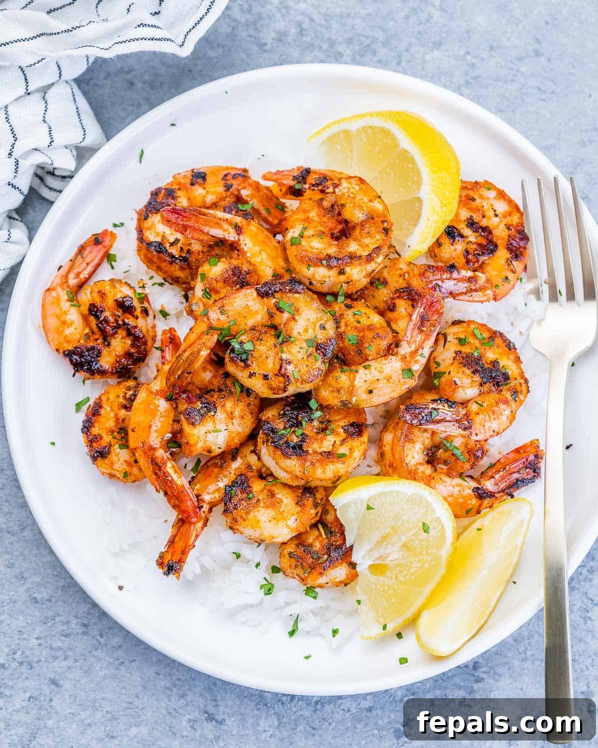 A top-down view of a pristine white plate, elegantly showcasing a generous serving of fluffy white rice topped with perfectly blackened shrimp, garnished with bright lemon wedges and a sprinkle of fresh green herbs.