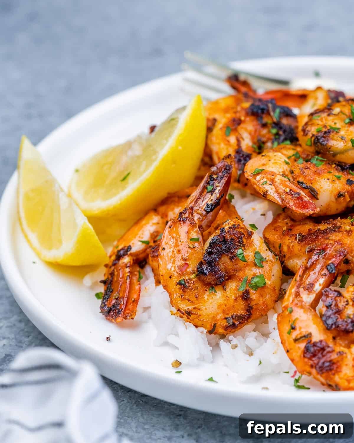 A beautifully presented white plate features succulent blackened shrimp arranged artfully over a bed of fluffy white rice, complemented by bright green lemon garnishes.