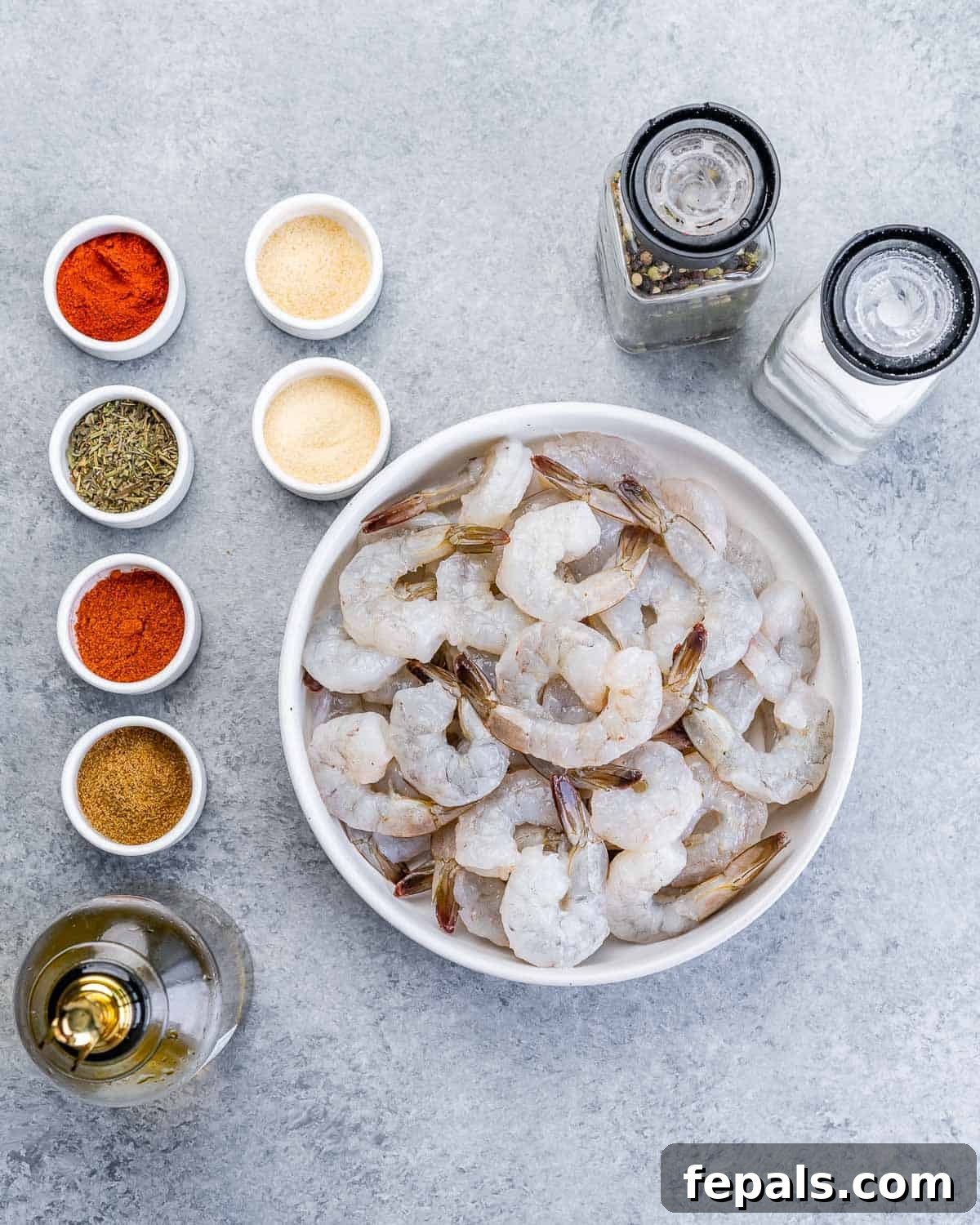 Close-up view of raw jumbo shrimp arranged alongside small, individual bowls filled with vibrant, various spices for the seasoning blend.